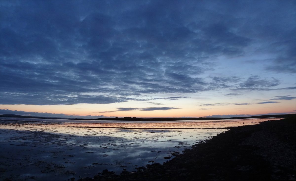 A wide summer sky over flat ground and water in Orkney